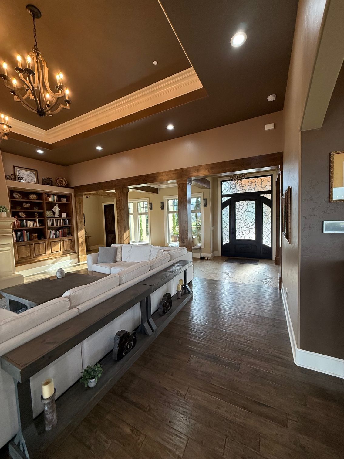 Spacious living room with high ceilings, gray sectional, dark wood floors, and large windows by the entryway