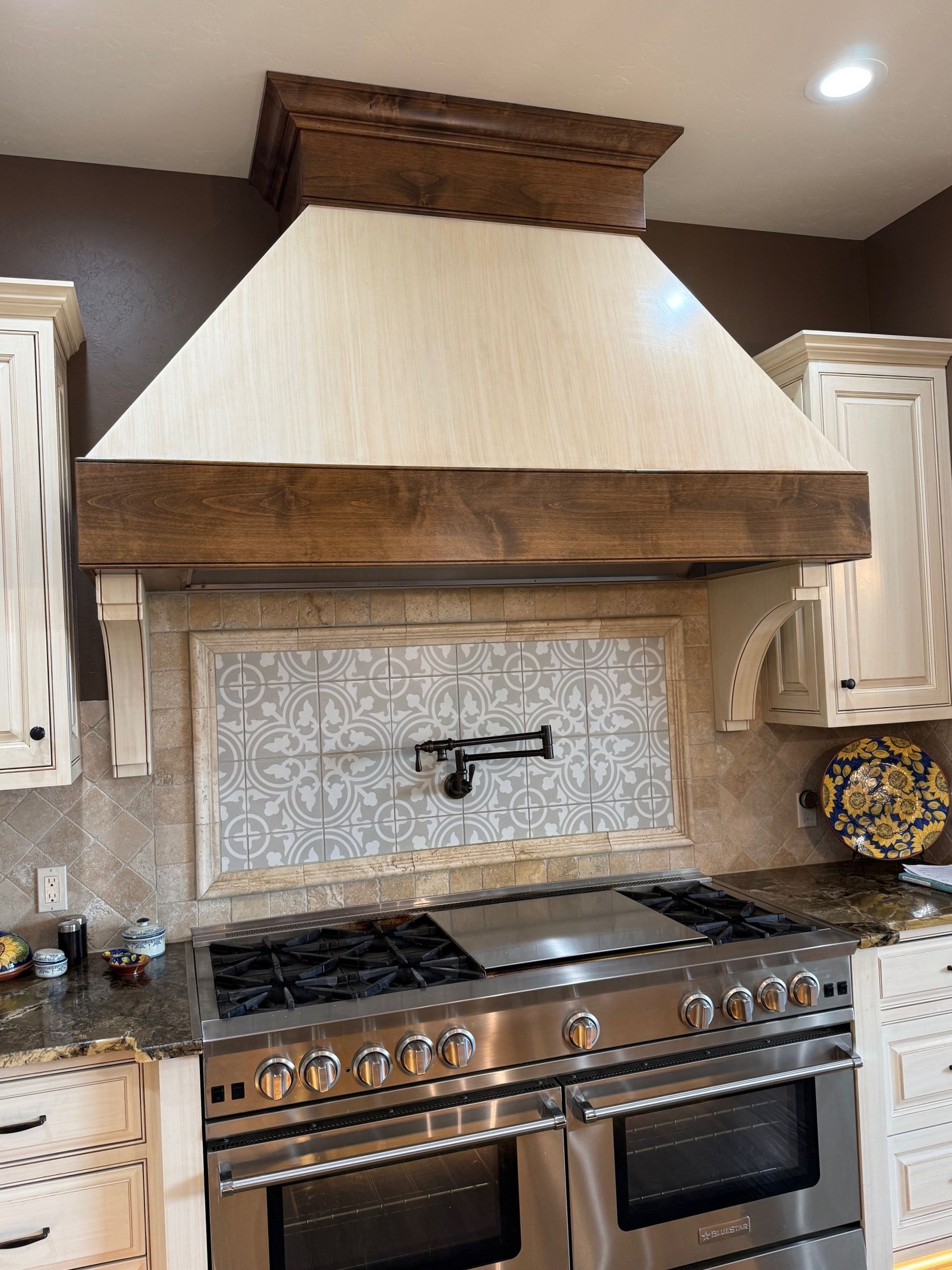 Kitchen stove with stainless range hood, mosaic tile backsplash, and white cabinets
