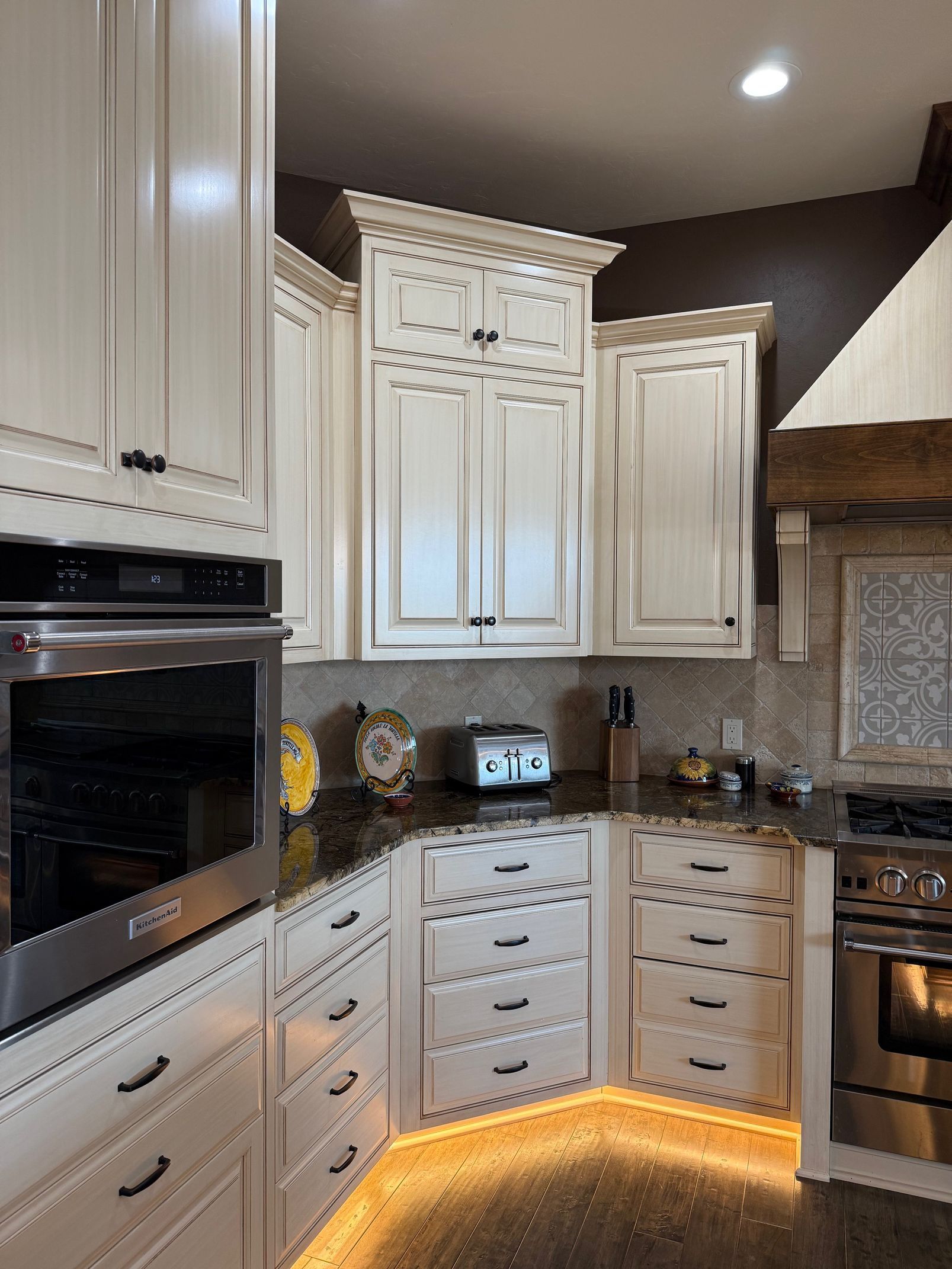 Elegant white kitchen with ornate cabinets, stainless oven, and warm under-cabinet lighting.