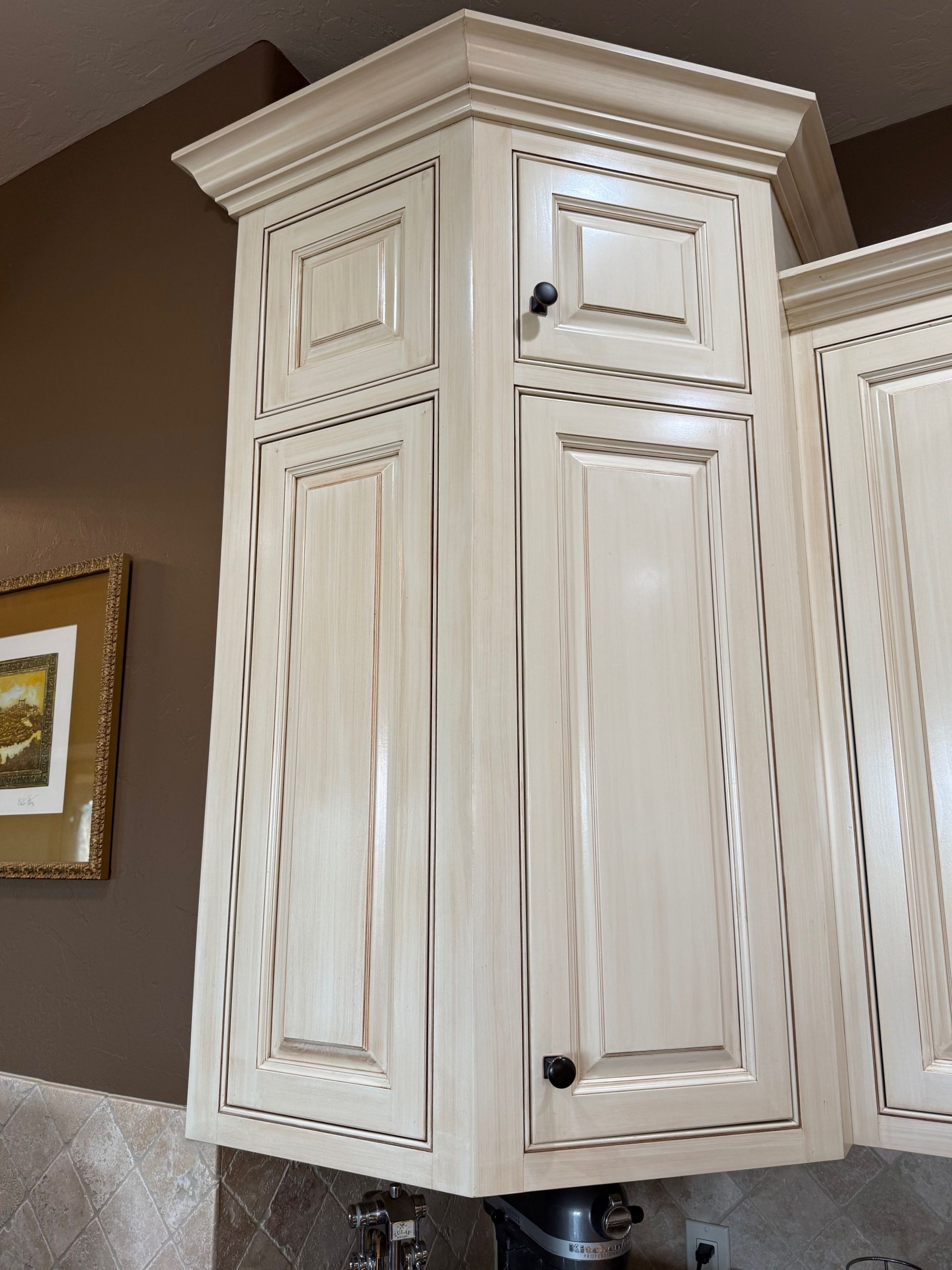 Cream-colored kitchen cabinet with crown molding and decorative trim on a beige wall.