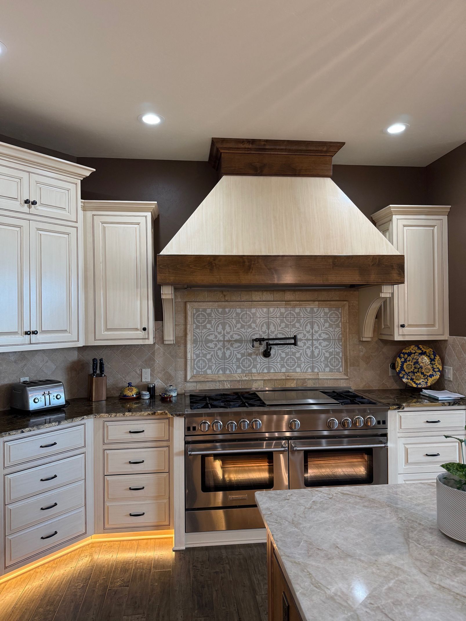 Modern kitchen with white cabinets, stainless steel stove, stone backsplash, and wood range hood