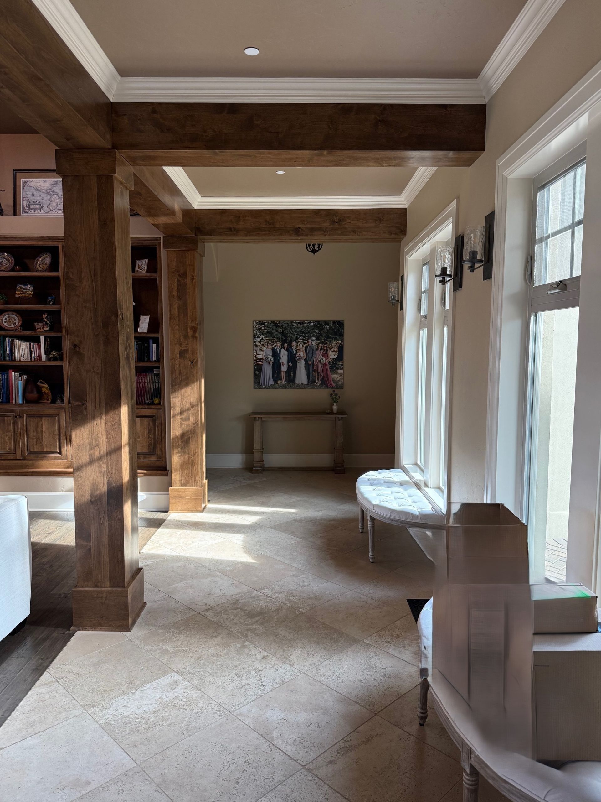 Wood-beamed hallway with windows, white benches, and a framed painting at the far end.