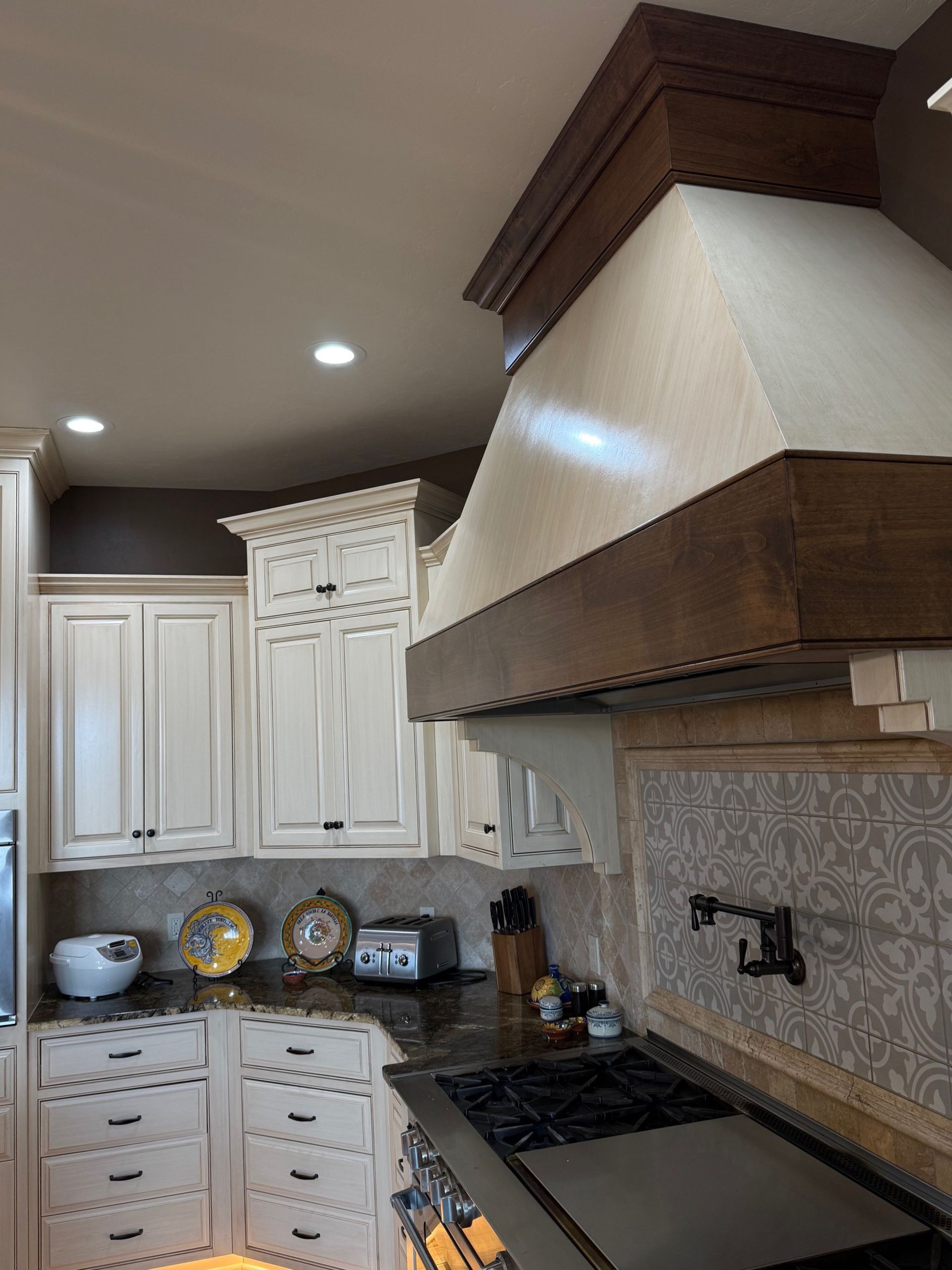 Compact kitchen with white cabinets, dark countertops, and a large stainless range hood over the stove.