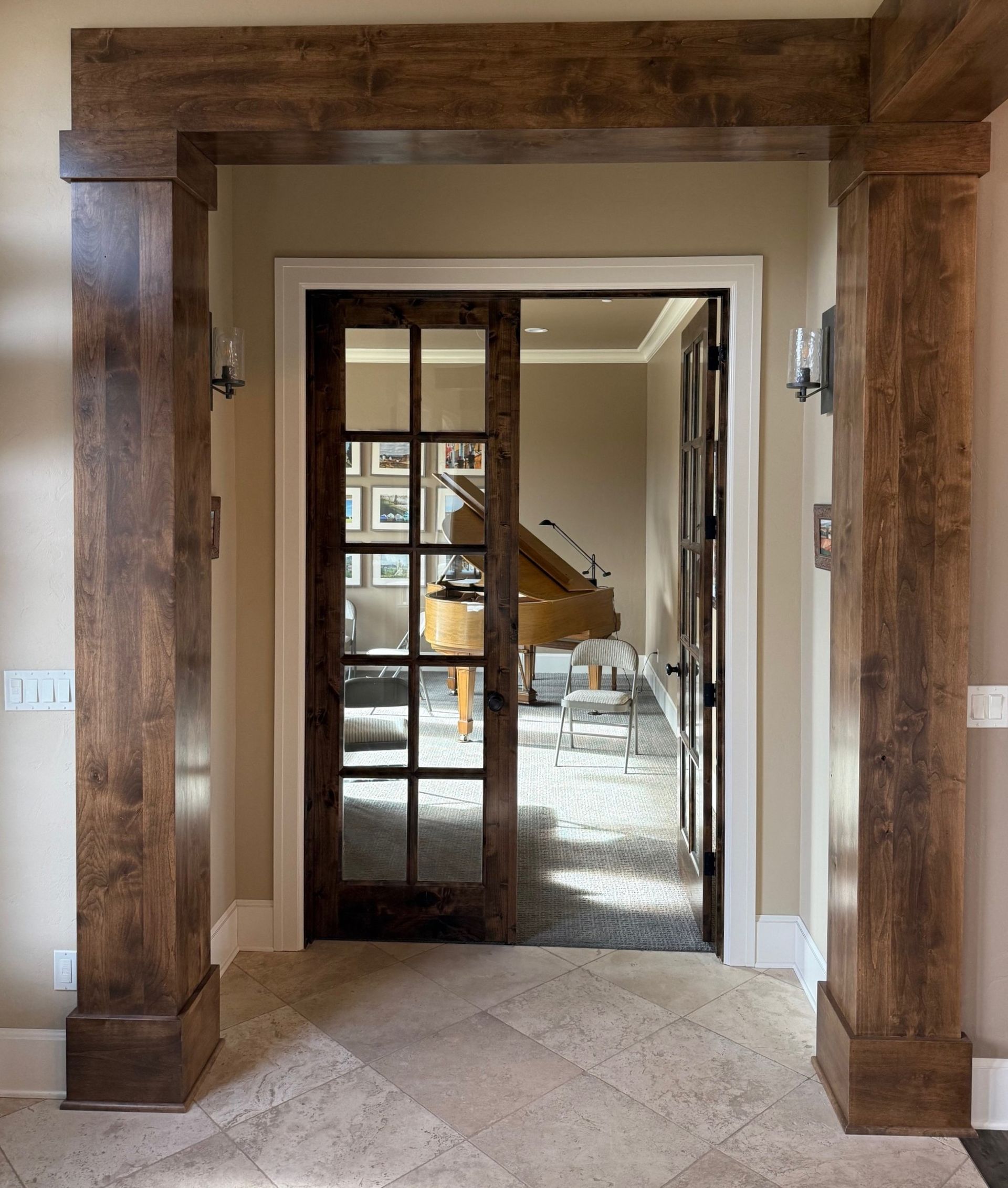 Wooden entryway framing glass French doors into a bright interior with a staircase beyond.