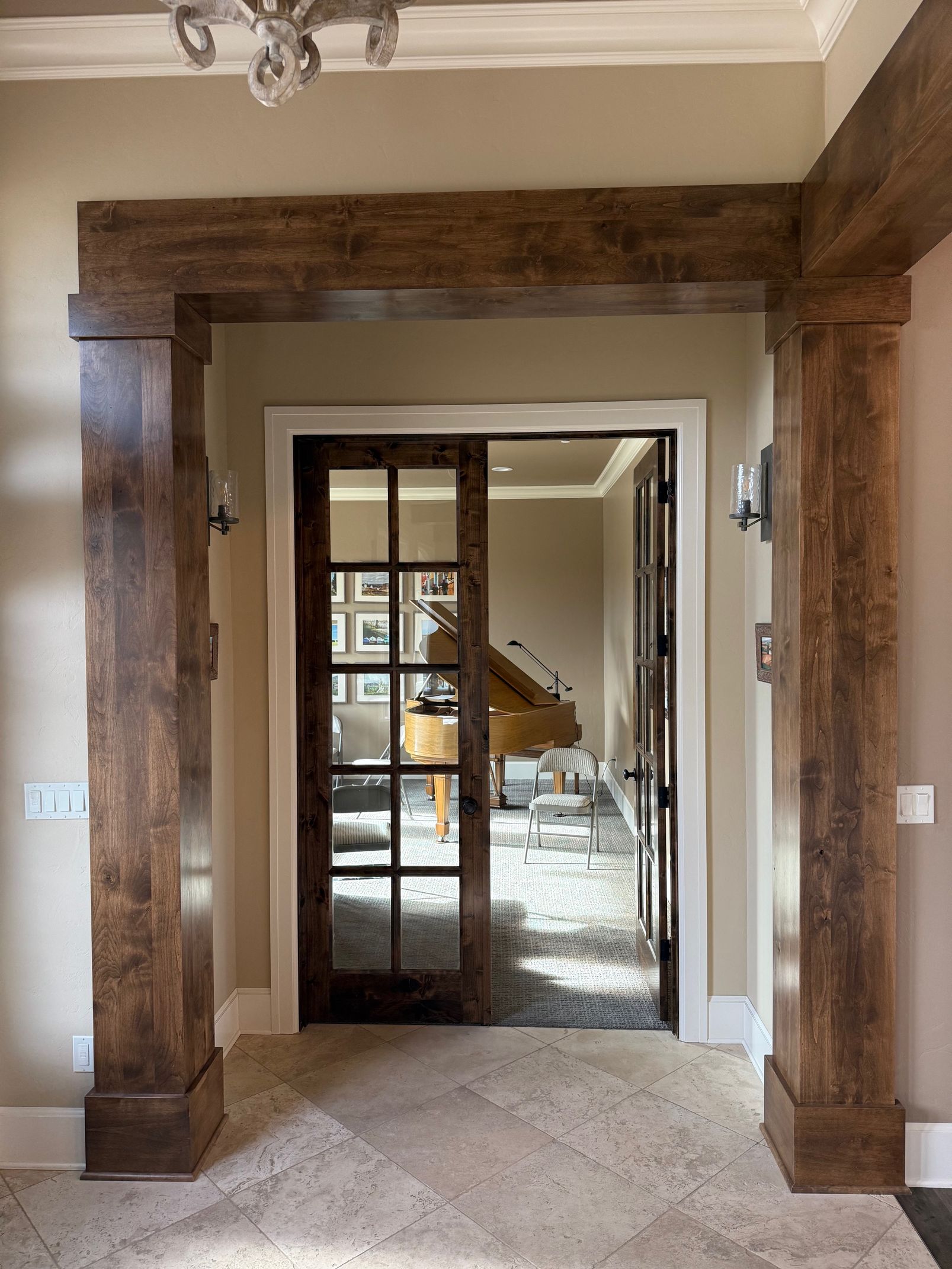 Interior doorway framed by rustic wood beams, leading into a bright room with glass doors and a staircase beyond