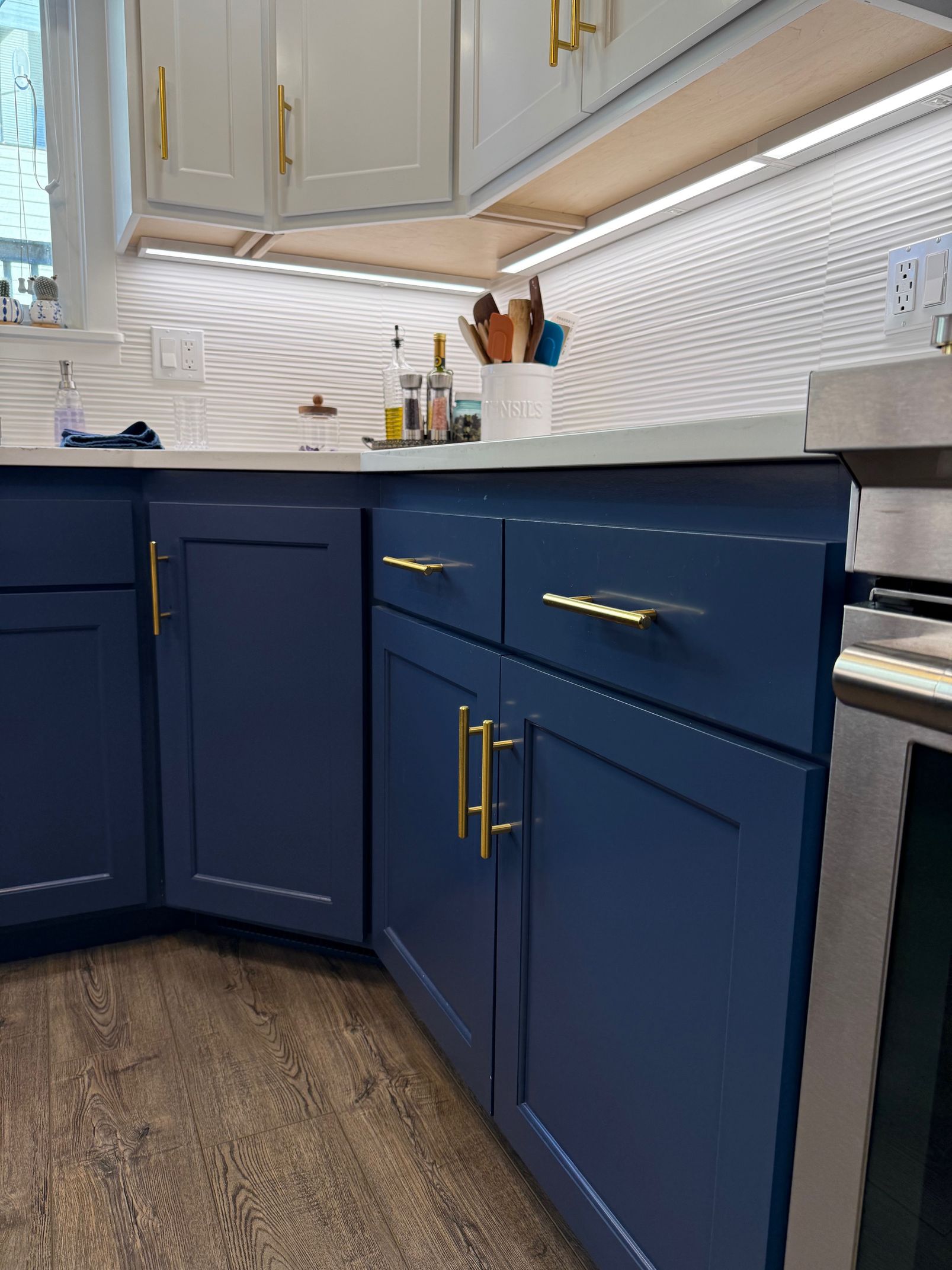 Blue kitchen cabinets with gold handles beneath a white mosaic tile backsplash and countertop.