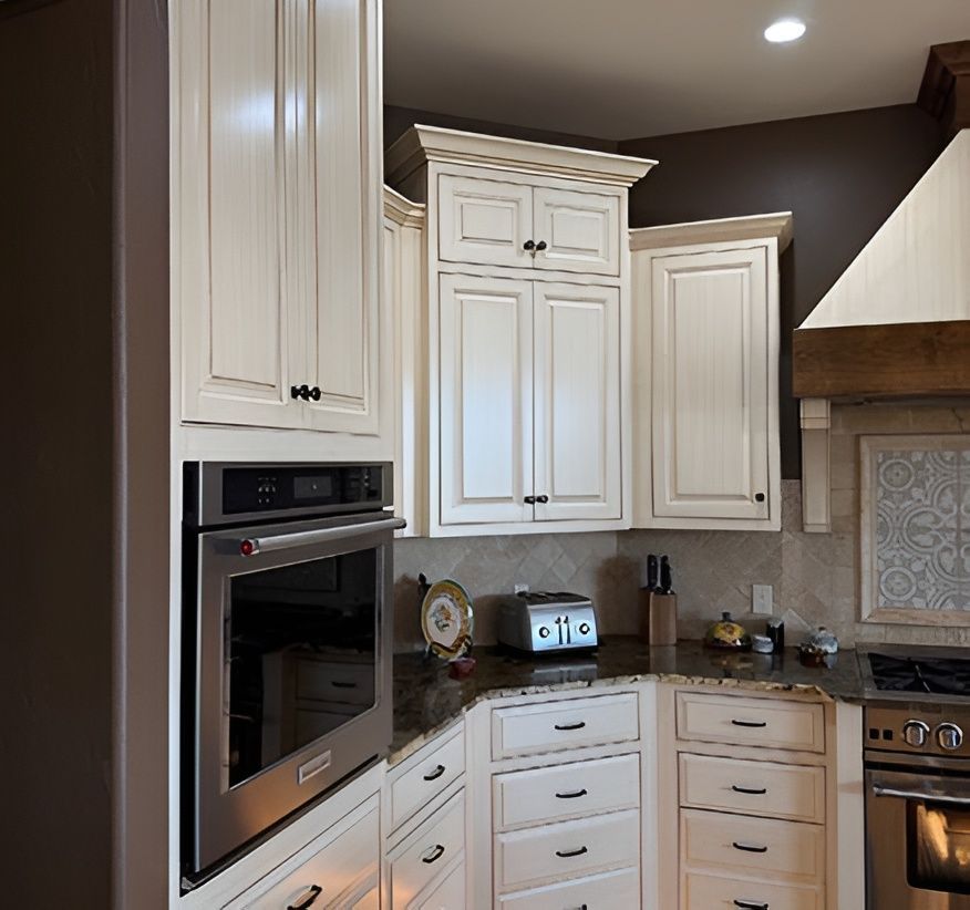 Bright kitchen corner with white cabinets, stainless oven, and dark granite countertops