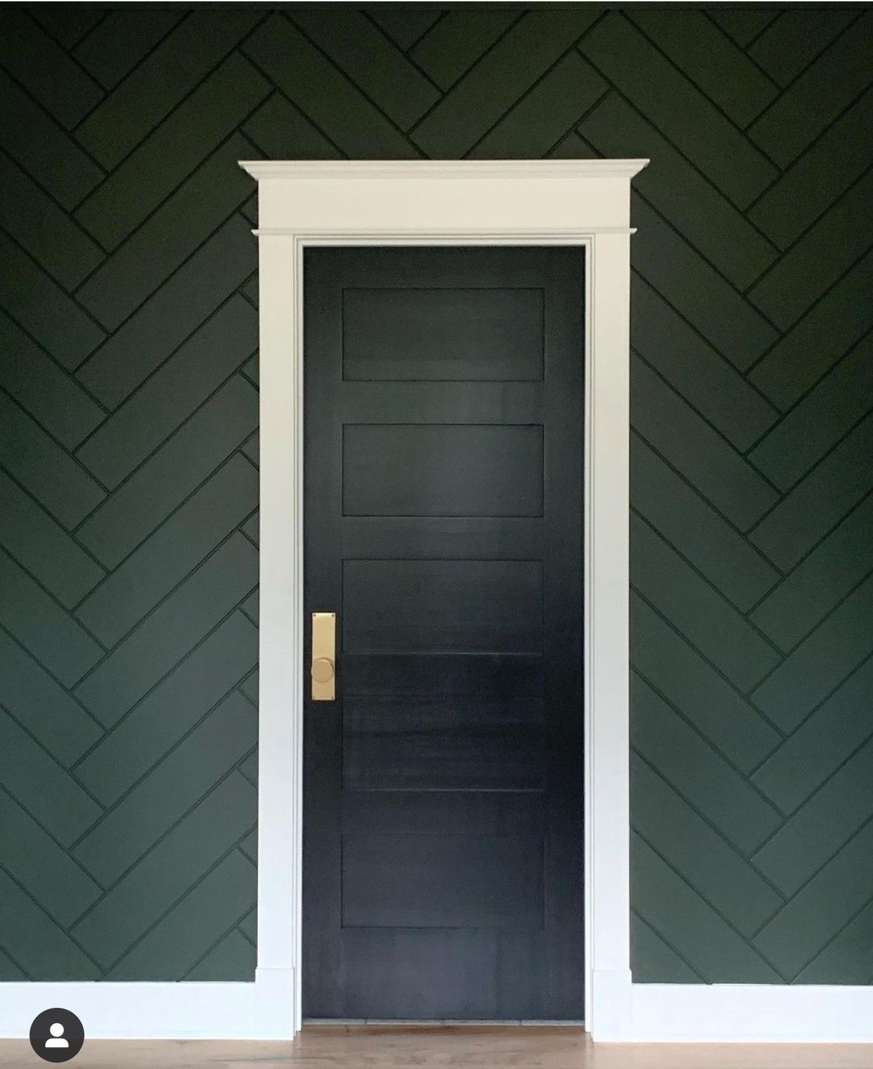 Black door with white trim set in dark green herringbone wall paneling