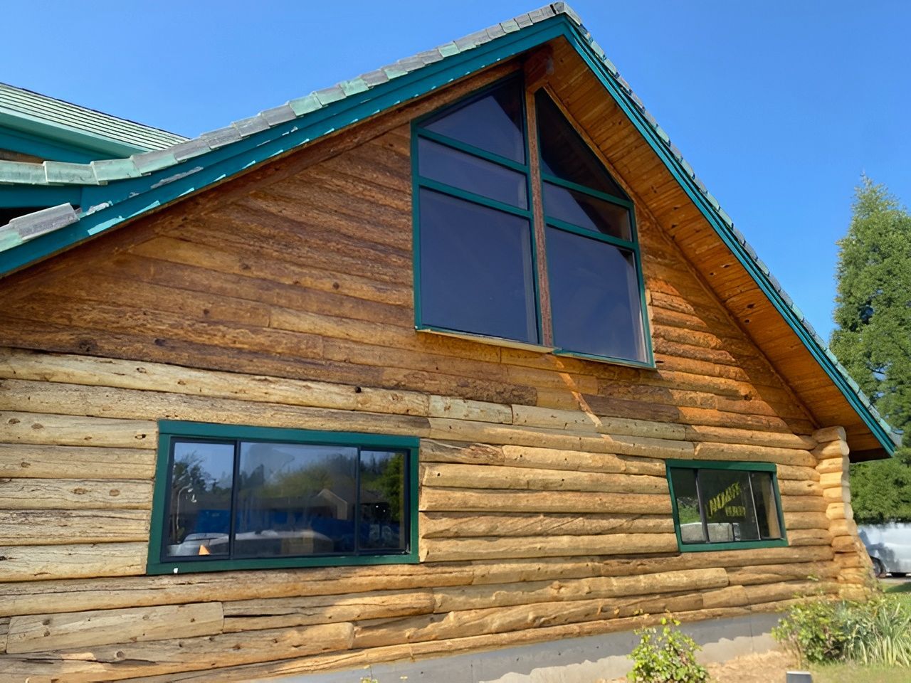 Wooden cabin exterior with green trim and large windows under a blue sky