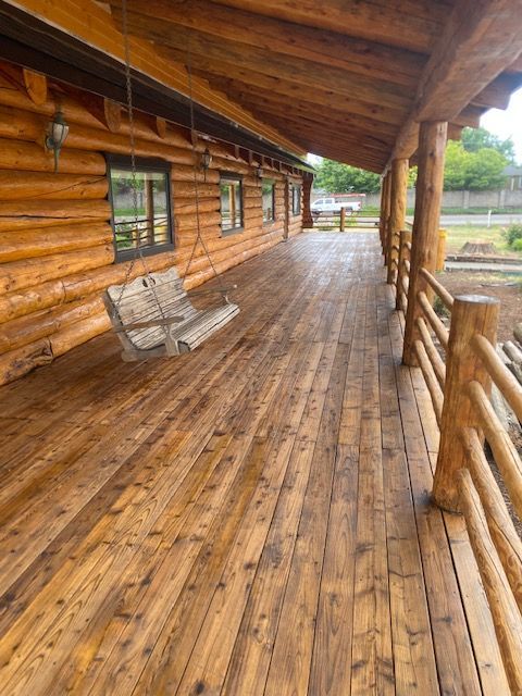 Covered wooden porch with log walls, railing, and a hanging bench swing on a wet floor.