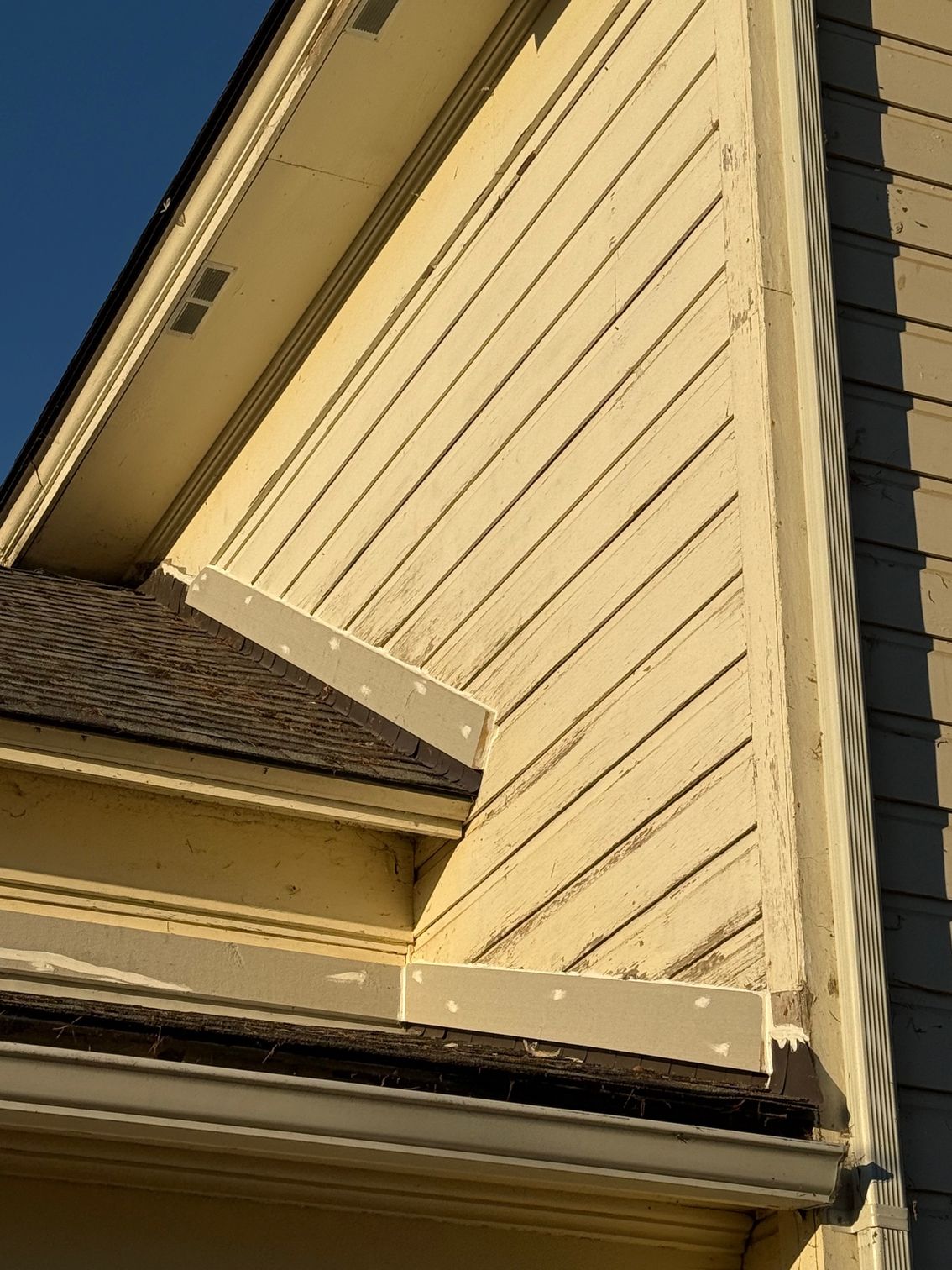 Beige house exterior with sloped roof and vertical siding against a blue sky