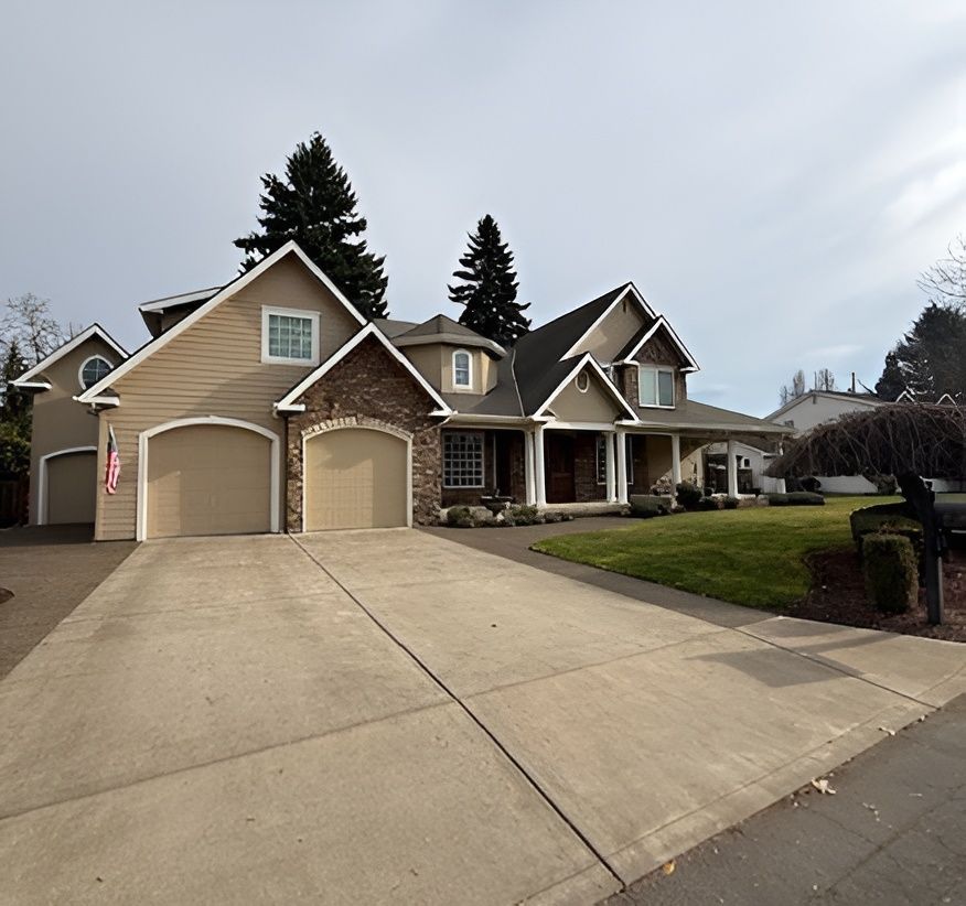 Suburban house with two-car garage, beige siding, and a wide concrete driveway under an overcast sky