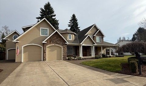 Large suburban house with two garages, beige siding, and a wide driveway on a cloudy day