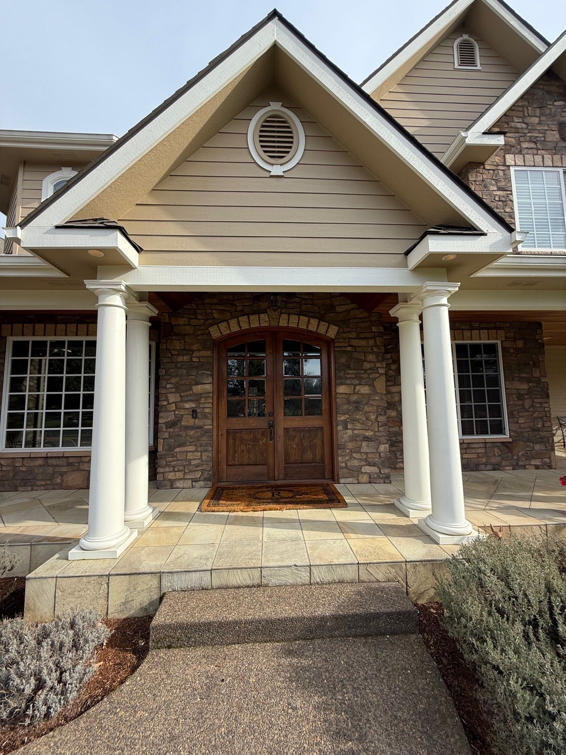Front entrance of a tan house with white columns, brick archway, and wooden double doors
