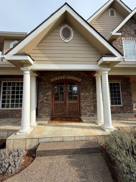 Front entrance of a beige house with white columns, brick arch, and wooden double doors.