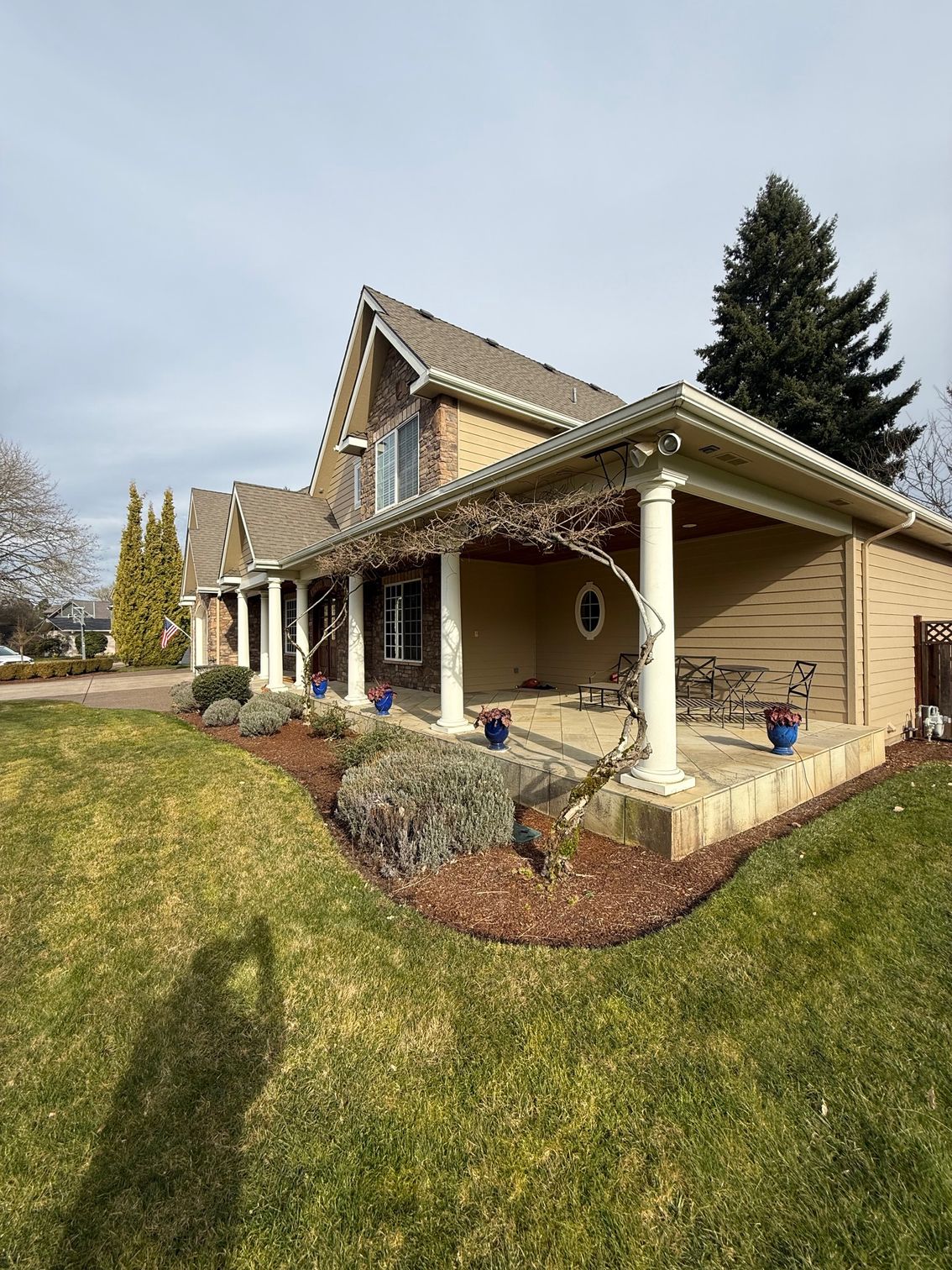 Suburban house with a covered porch, beige siding, and a sloped green lawn under a cloudy sky
