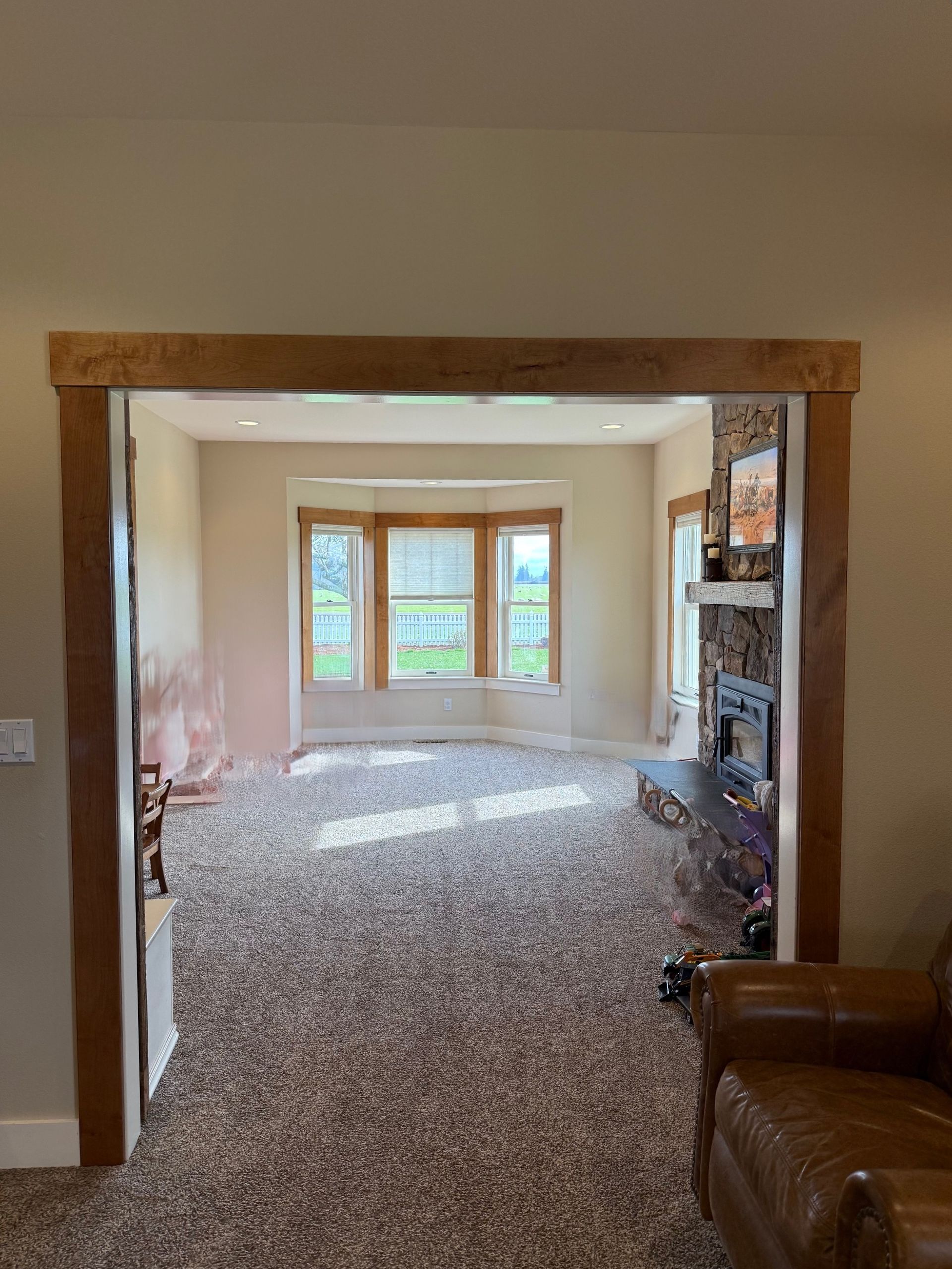 Carpeted living room viewed through a doorway, with a large window seat and brown leather chair.