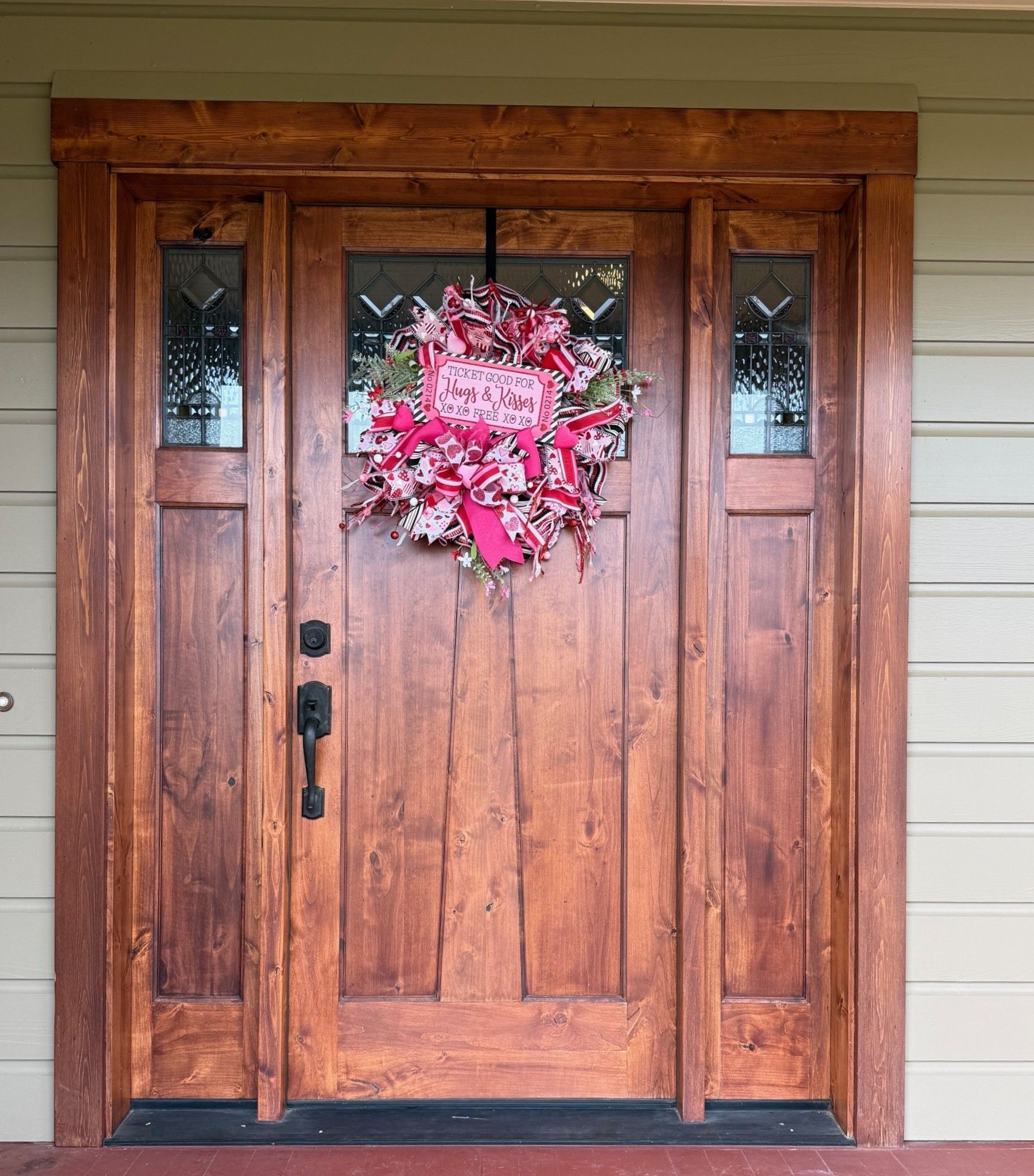 Wooden front door with pink wreath and sidelights on a house porch