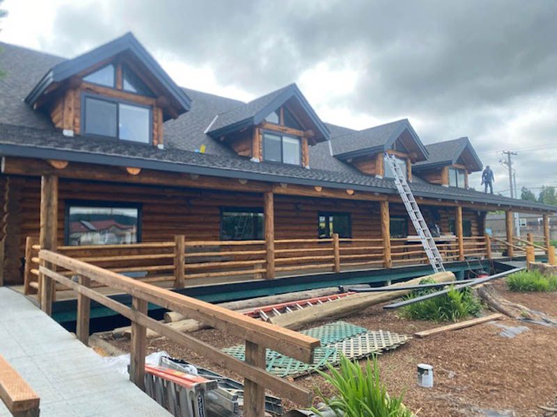 Wooden log cabin with dormer windows and a front ramp under construction on a cloudy day
