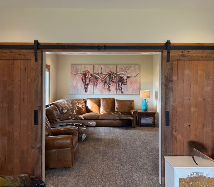 Cozy living room with brown leather sectional, rustic barn doors, and abstract wall art.