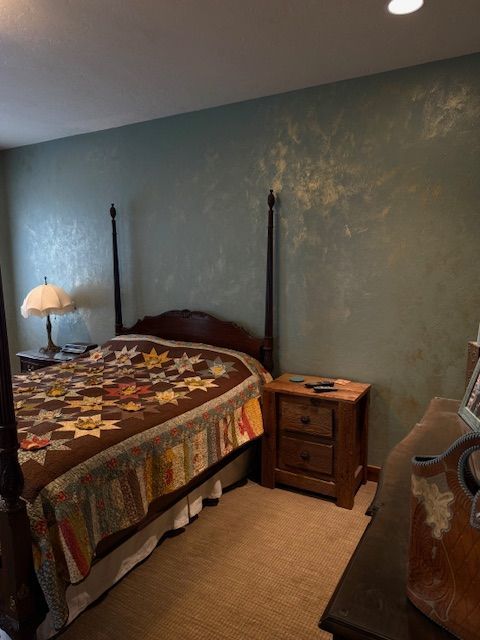 Bedroom with a bed, nightstand, lamp, and dresser against blue-green walls.