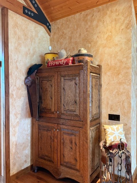 Wooden armoire in a rustic corner with warm walls, decor on top, and a small chair beside it