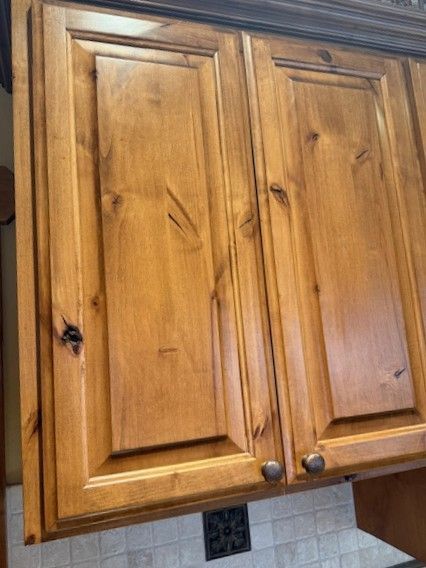 Wooden kitchen wall cabinets with brass knobs above a tiled backsplash