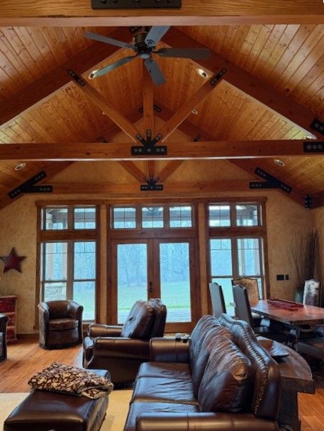 Cozy living room with vaulted wood ceiling, ceiling fan, leather sofas, and large windows overlooking a lake