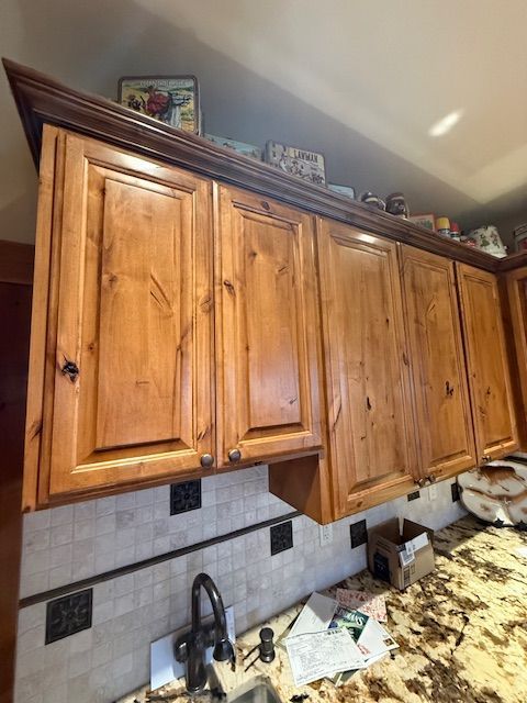Wooden kitchen cabinets above a tiled backsplash and countertop with a sink and faucet.