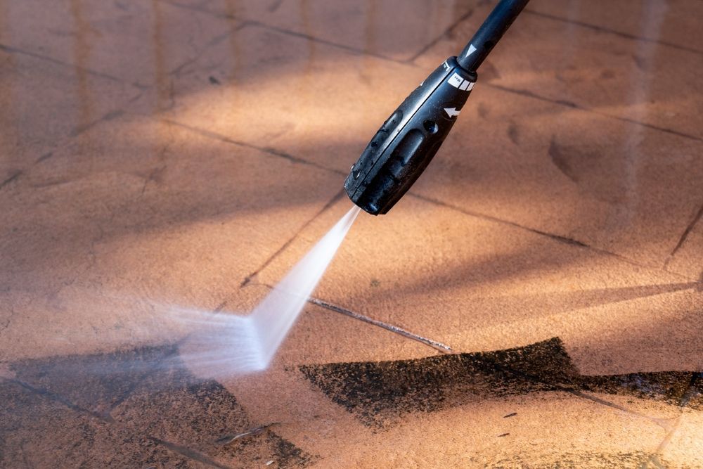 Pressure washer spraying water onto a tan tiled surface, cleaning away dirt.