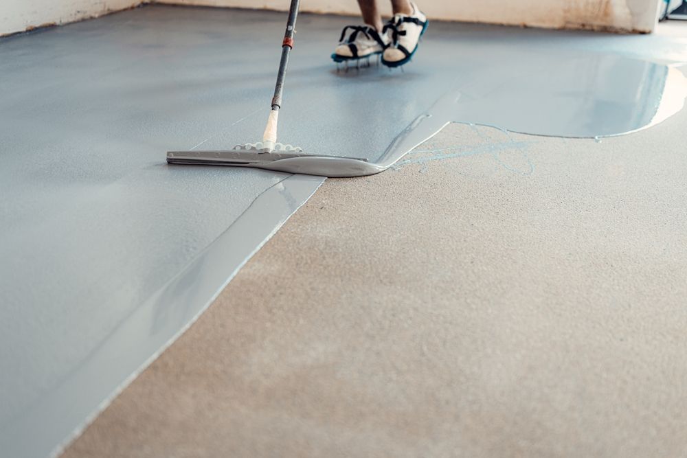 Worker smoothing gray floor coating with a squeegee in a room under construction