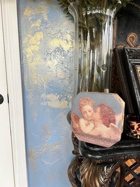 Decorative display shelf with a cherub plaque beside a black vase and framed photo, against a blue wall.