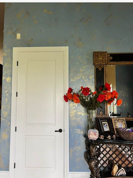 White door beside blue wall and ornate mirror with flowers on a dark console table