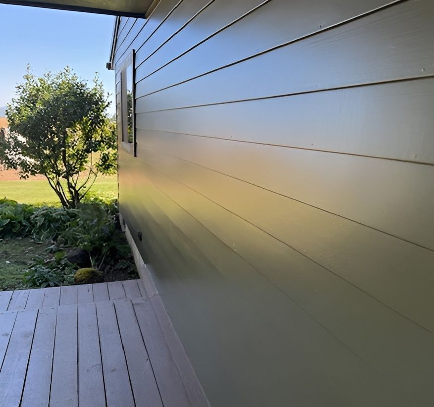 Side view of a house with beige siding, a wooden deck, and a grassy yard with trees nearby.
