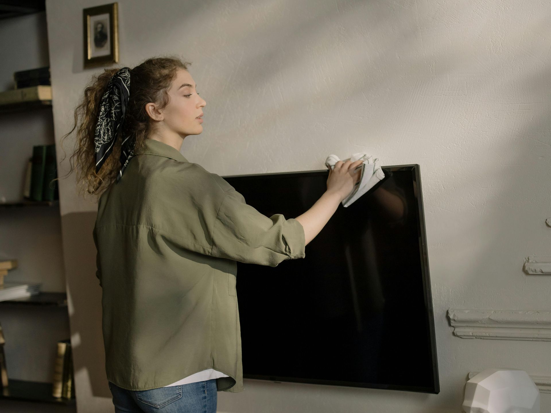 A woman is cleaning a flat screen tv with a cloth.