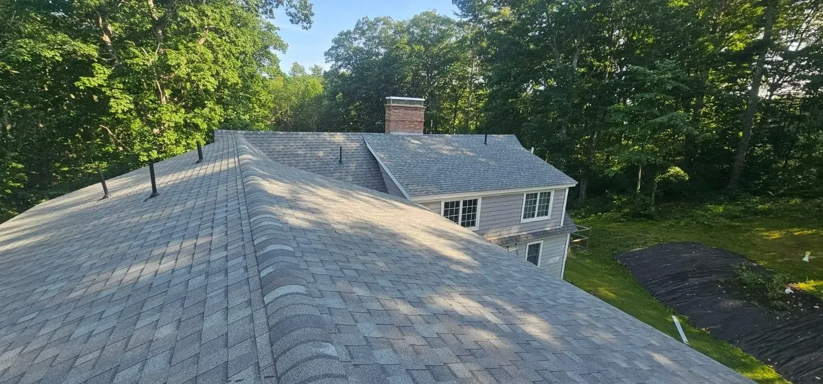 A roof of a house with a chimney and trees in the background.