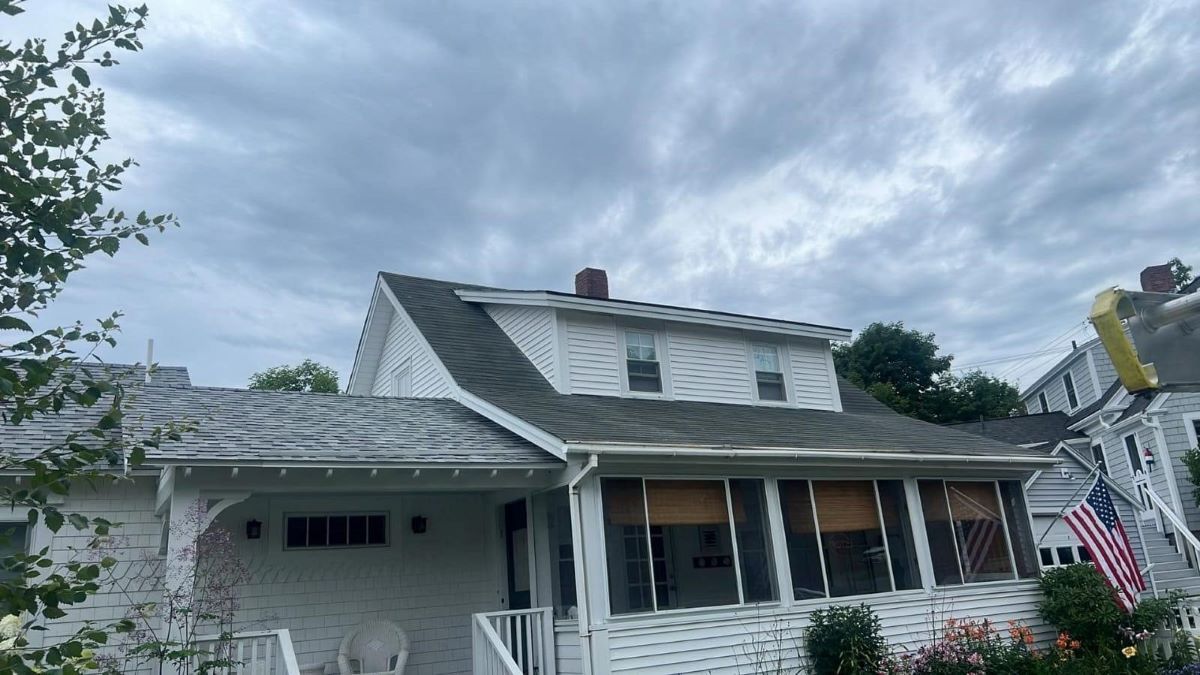 A white house with a gray roof and a large screened in porch.