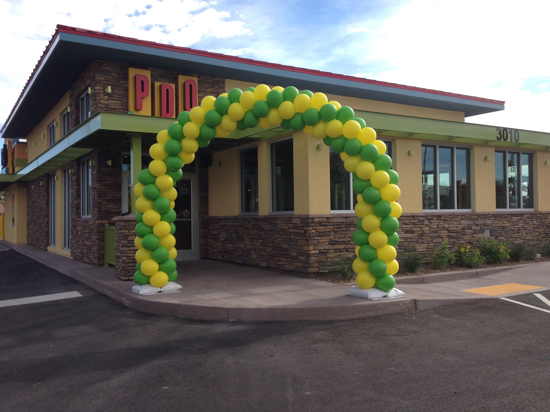A yellow and green balloon arch in front of a building