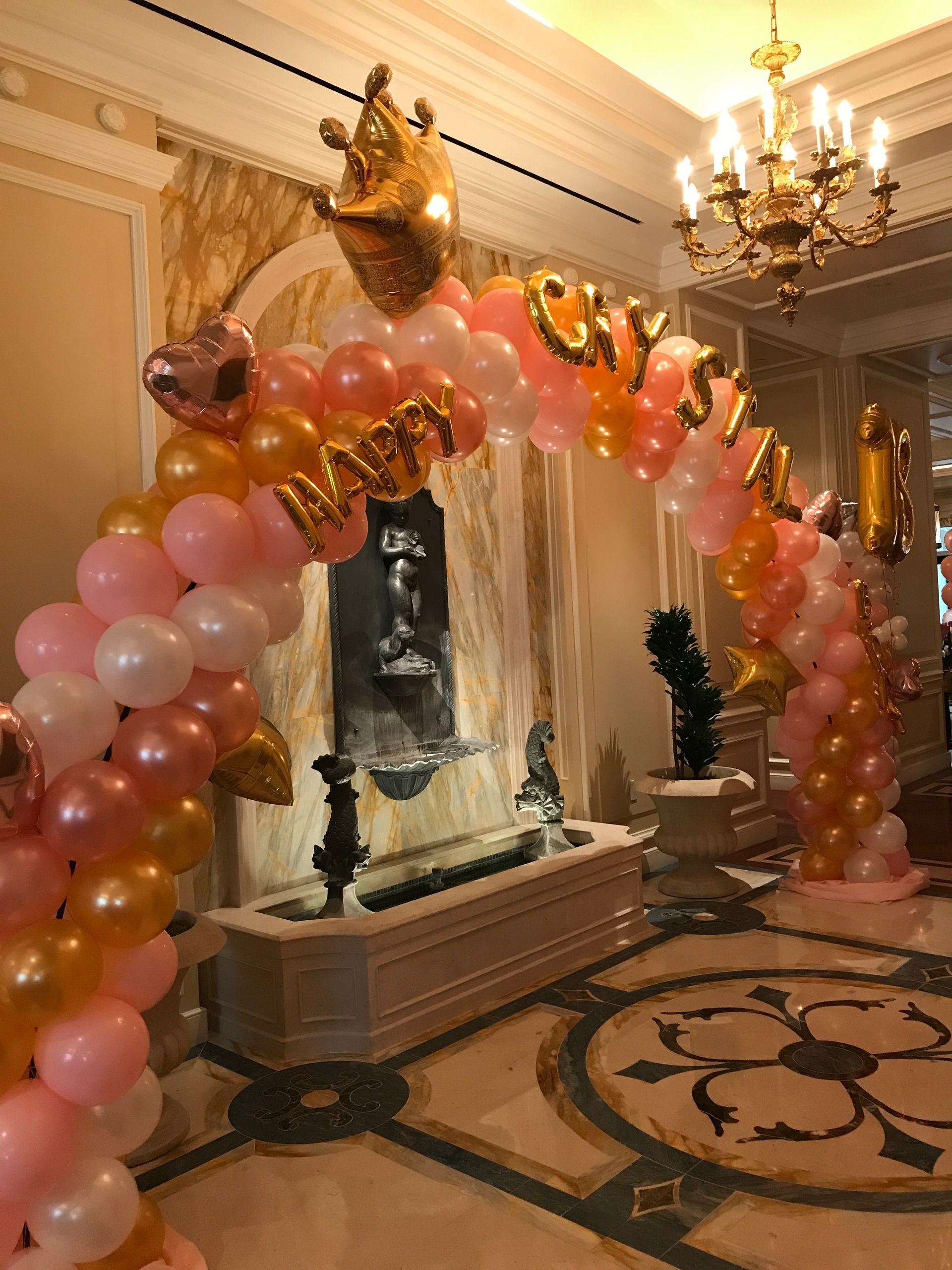 A pink and gold balloon arch with the word happy on it