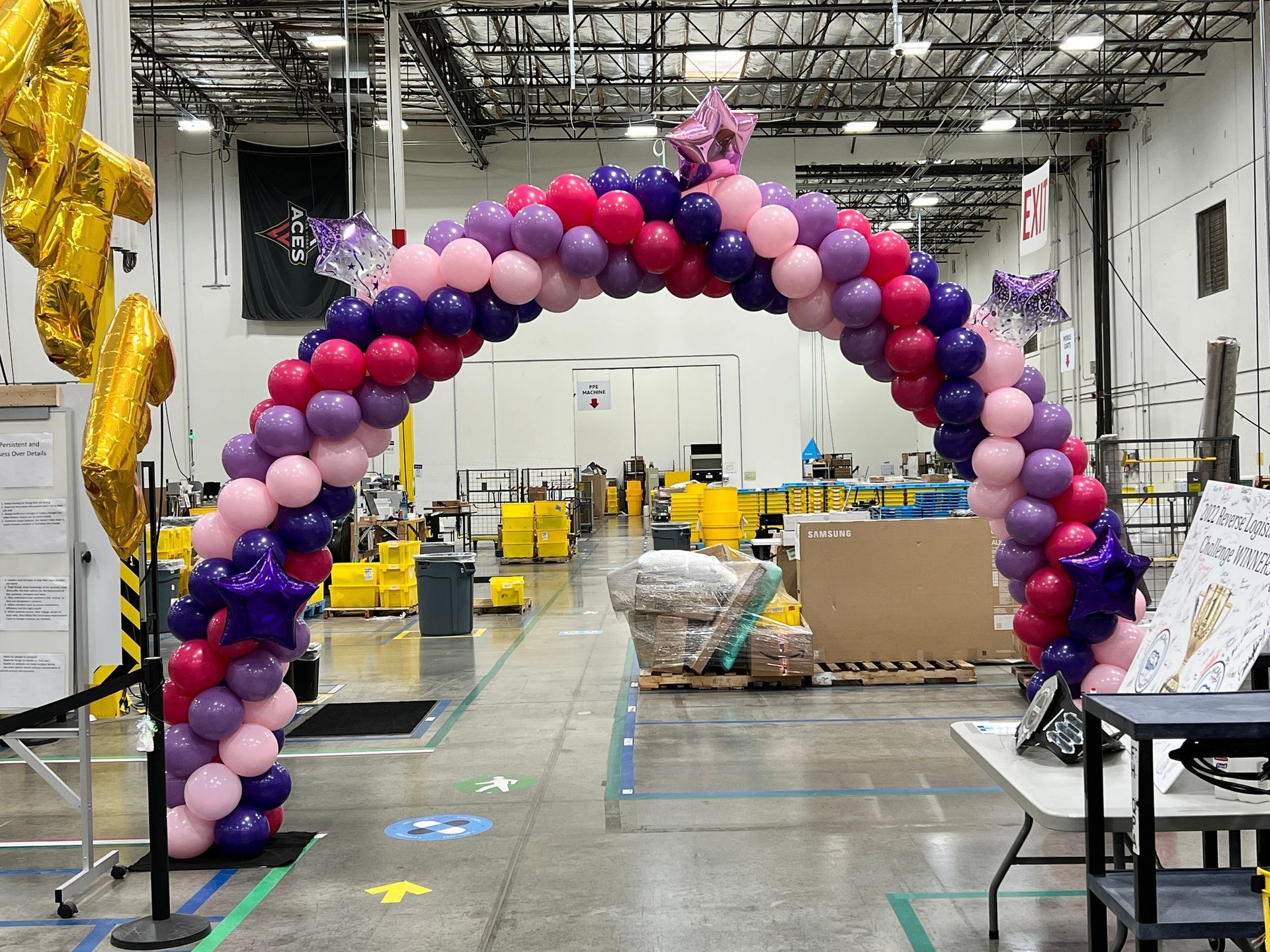 A large arch made of pink and purple balloons in a warehouse.