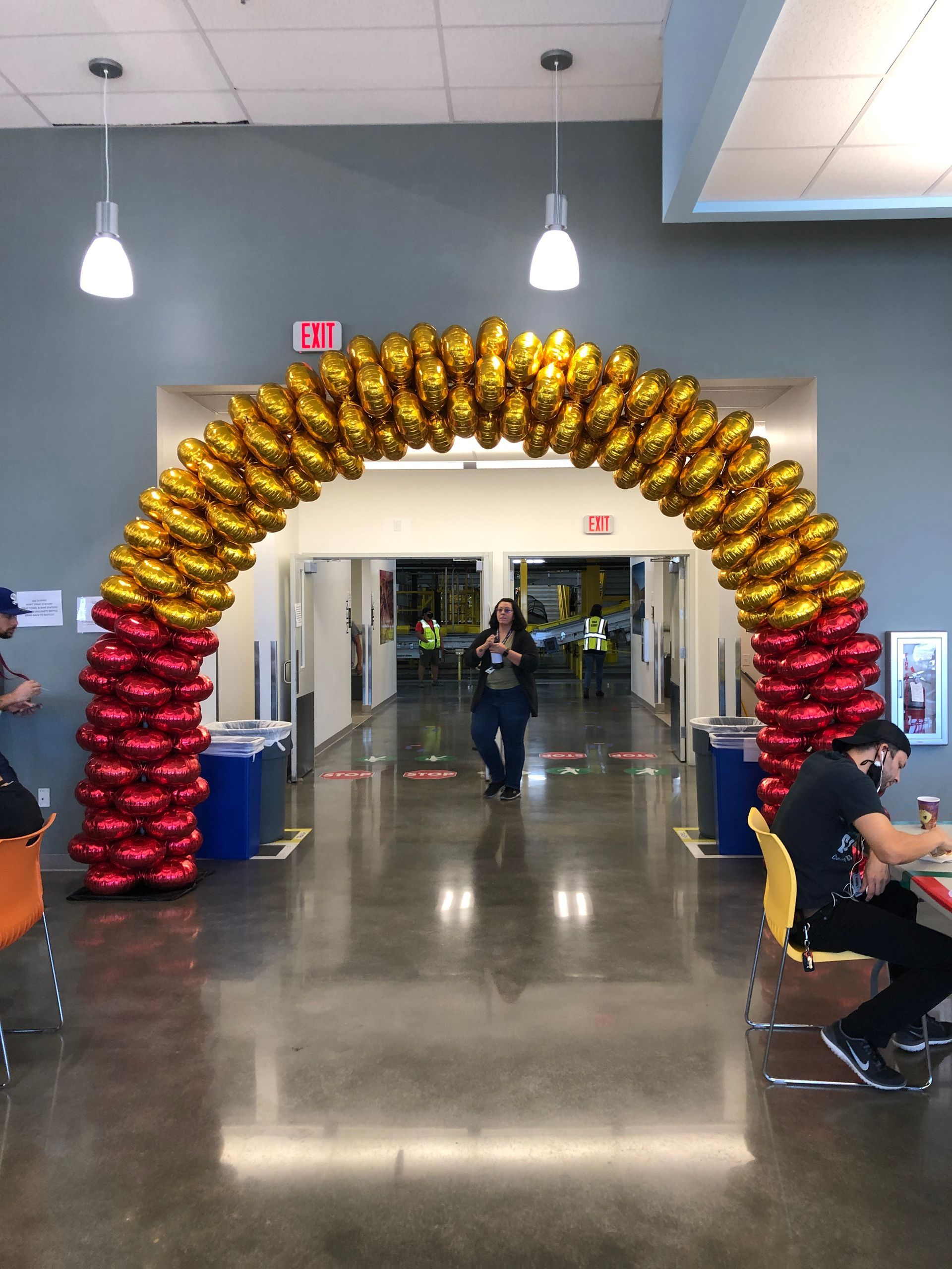 A large arch made of red and gold balloons in a hallway