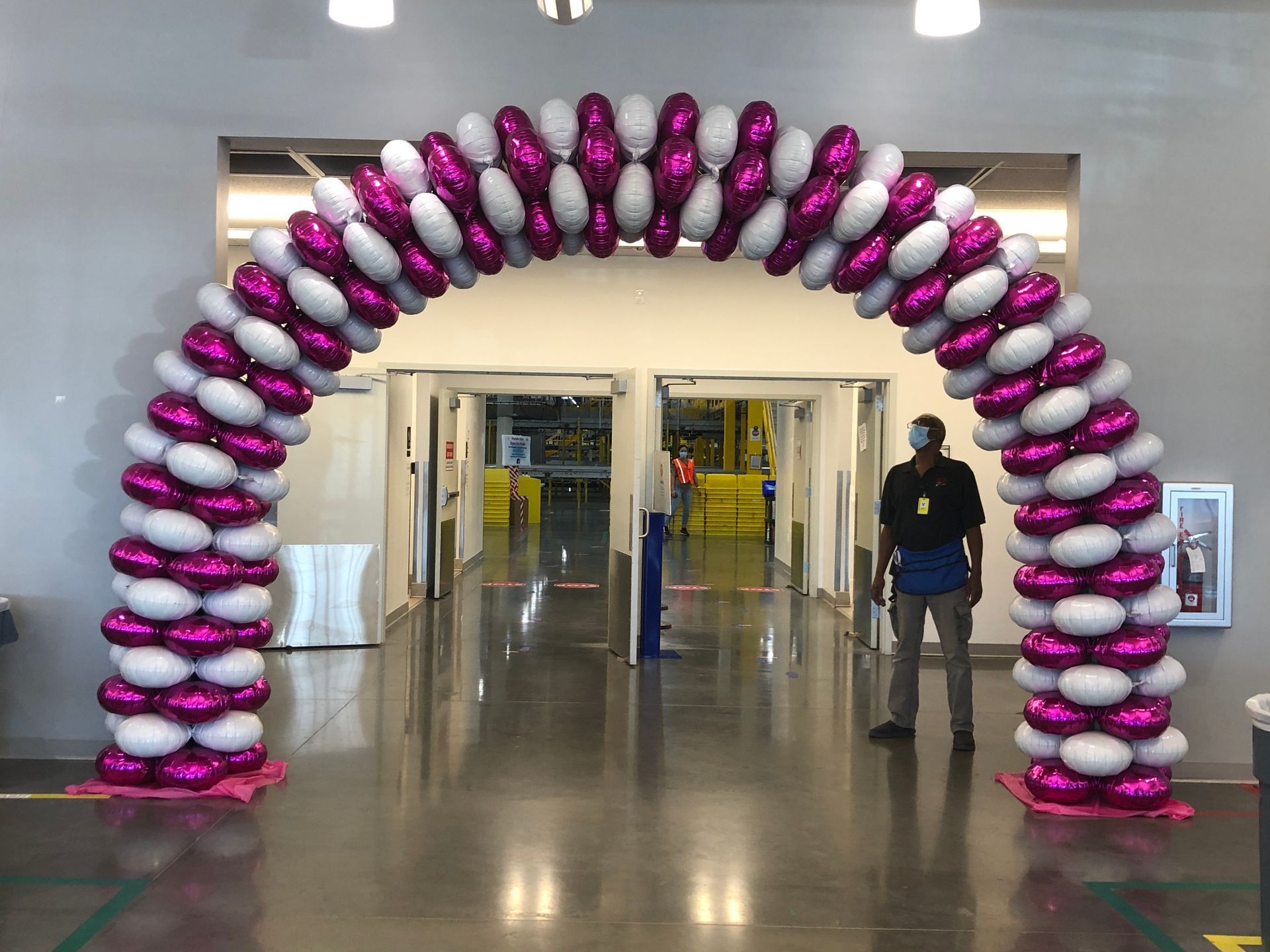 A man is standing under an arch made of pink and white balloons.