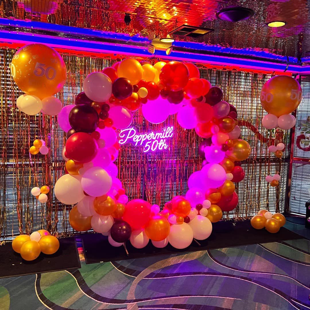 A room filled with balloons and a neon sign that says peppermill 30th.