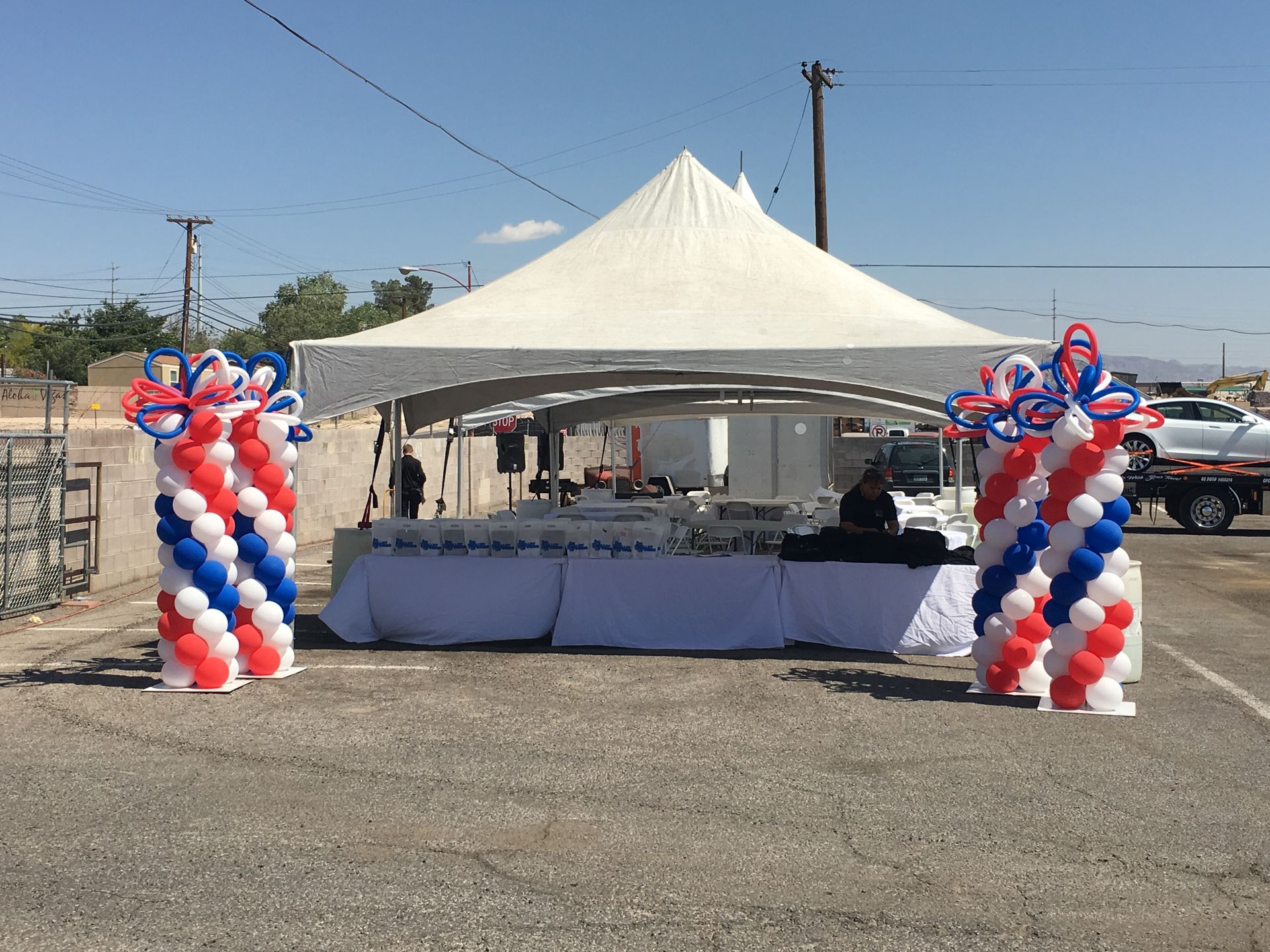 A white tent is surrounded by red , white and blue balloons.
