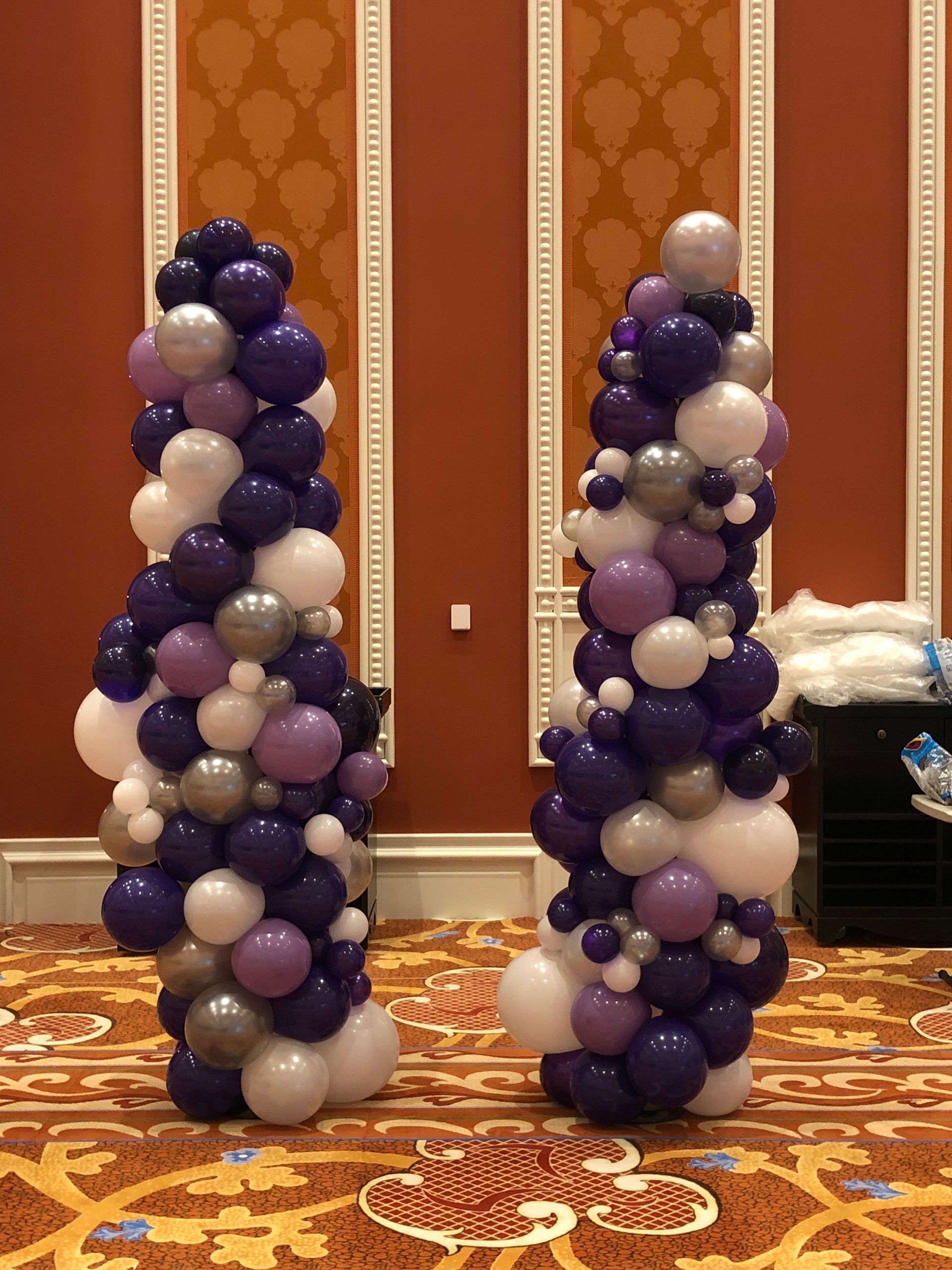 Two columns made of purple , white , and silver balloons in a room.