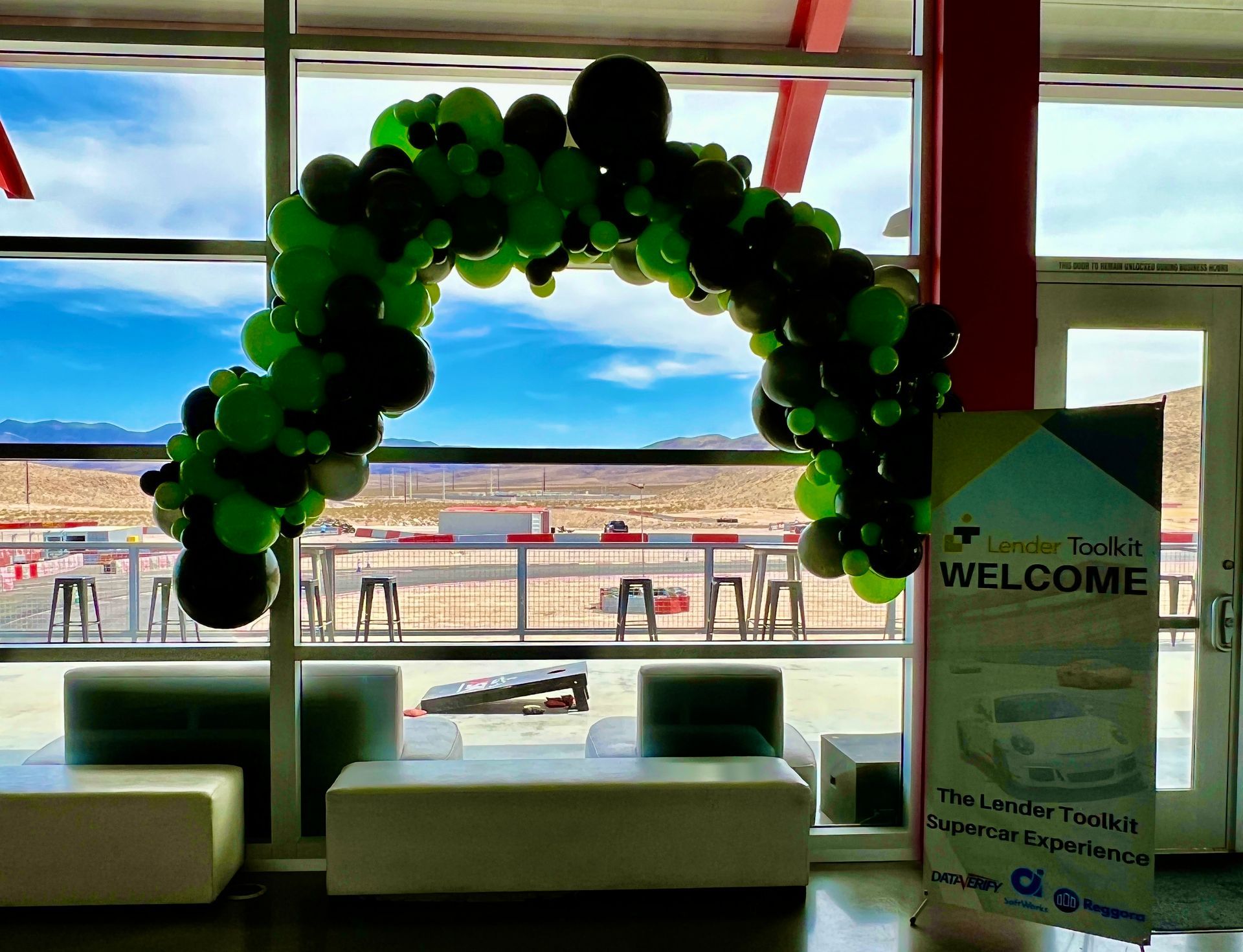A green and black balloon arch in a room with a welcome sign.