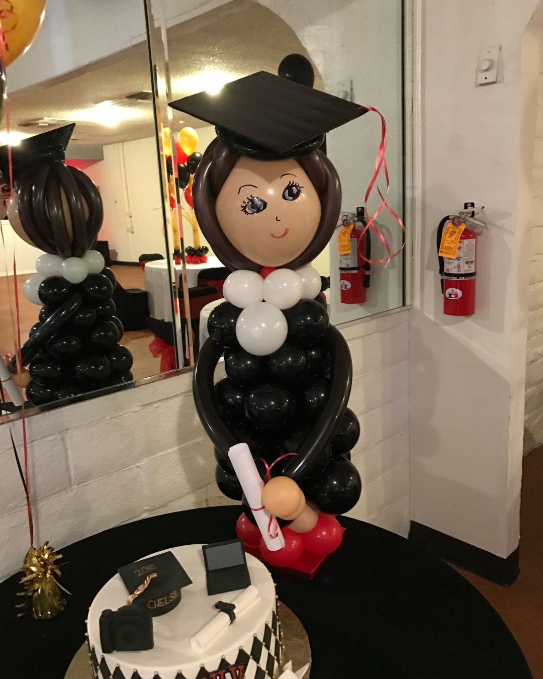 A balloon sculpture of a girl in a graduation cap and gown holding a diploma