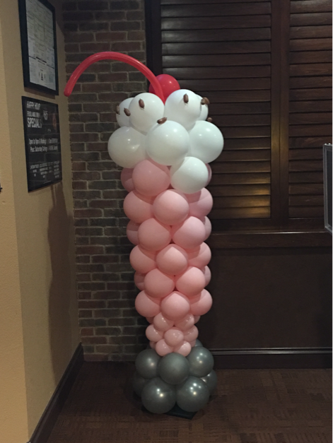 A pink and white balloon tower with a cherry on top