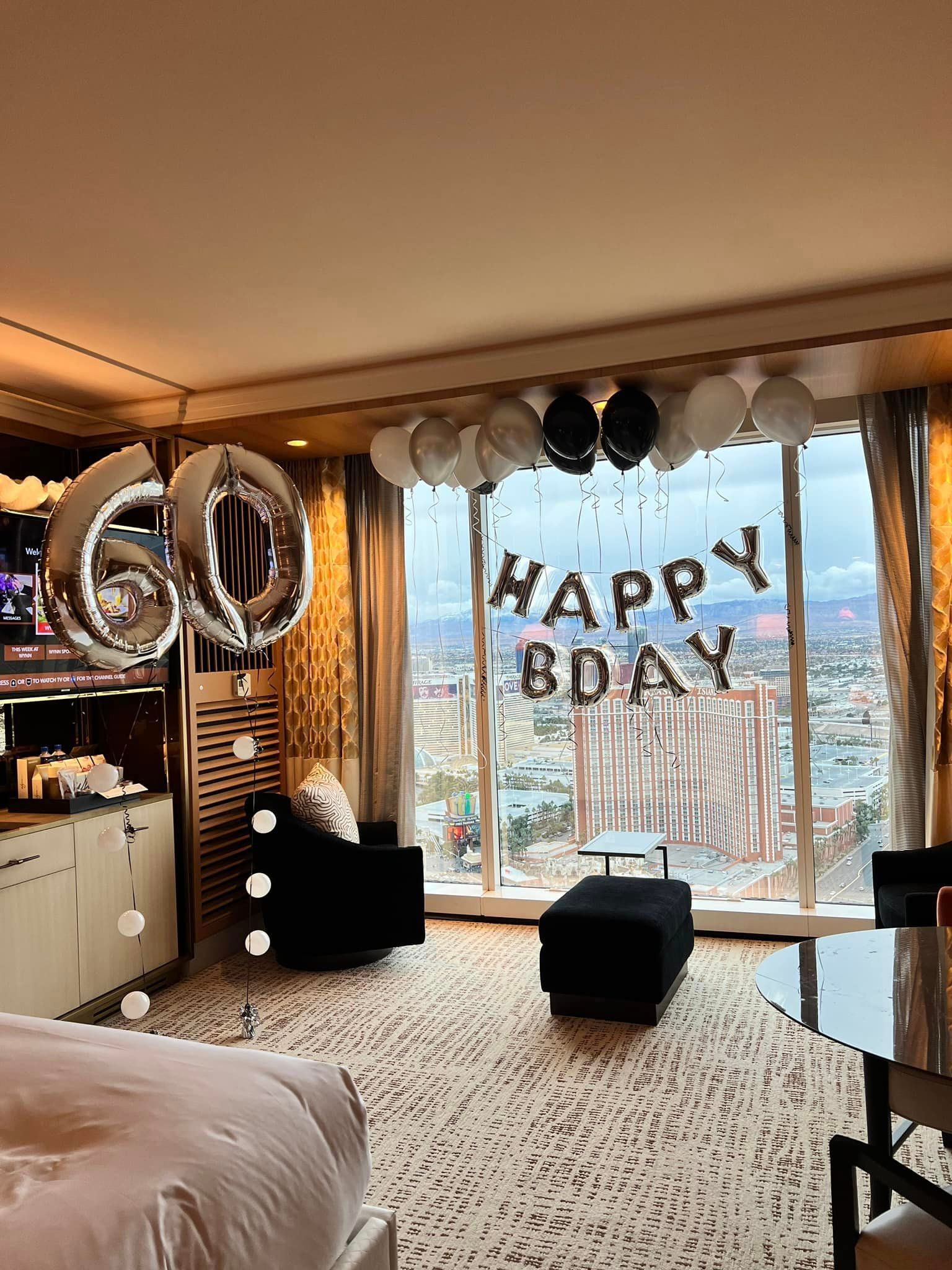 A hotel room decorated for a birthday with balloons and a bed.