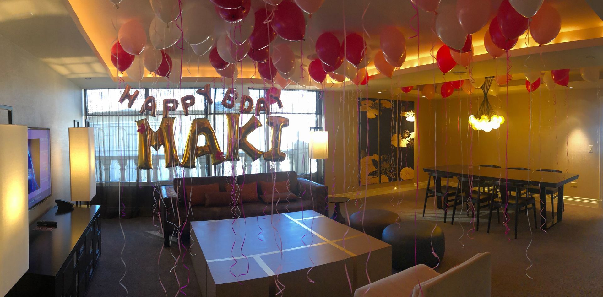 A living room with balloons hanging from the ceiling and a sign that says happy birthday maki